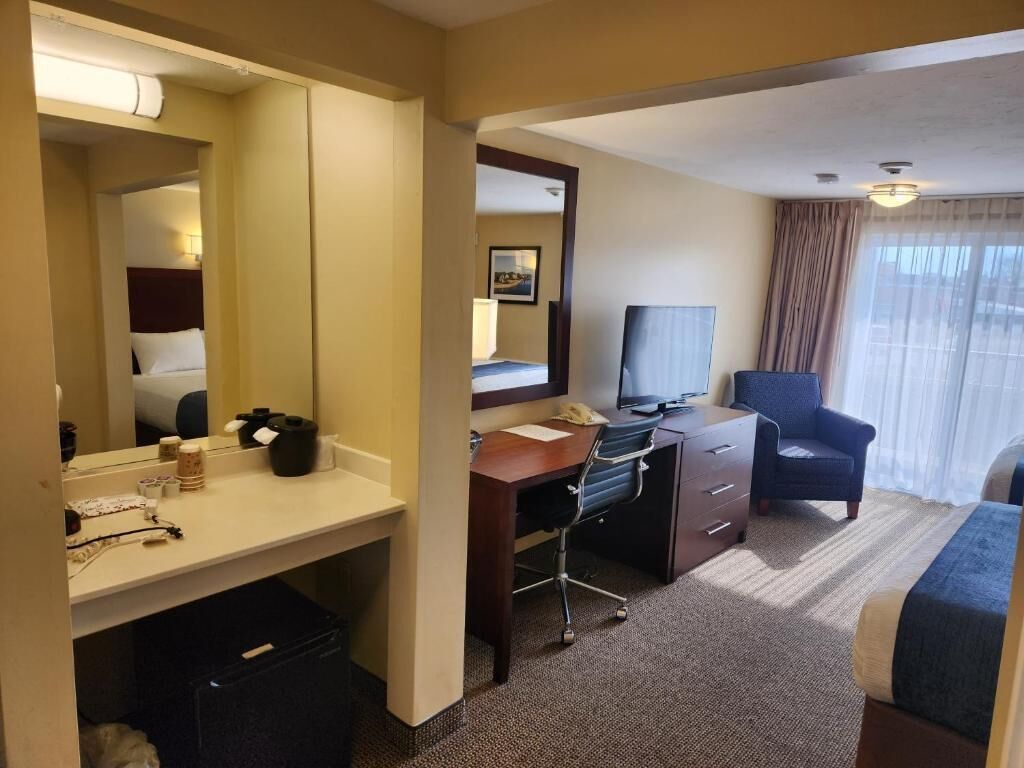 A hotel room with a bed, a desk with a computer, a chair, and a large window with curtains.
