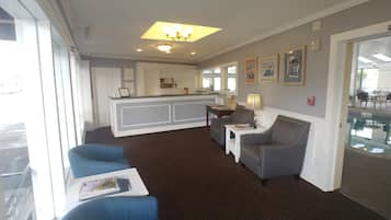 A hotel lobby with a reception desk, seating area, and a view of the pool.