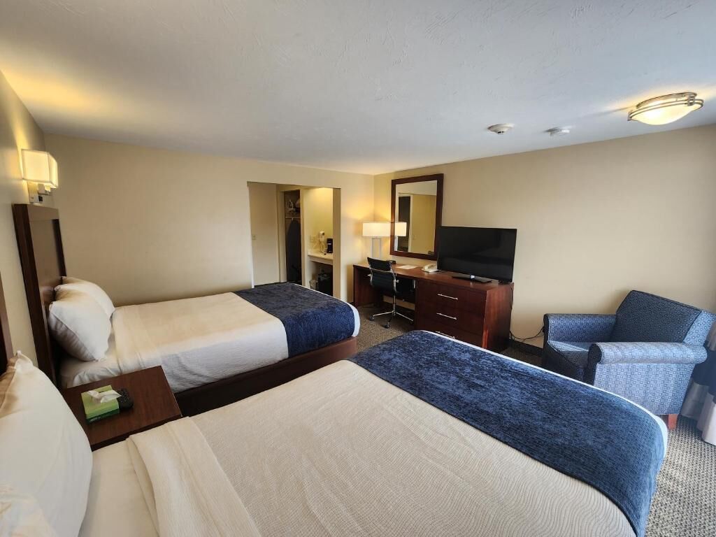 A hotel room with two beds, a desk with a TV, a chair, and a mirror.