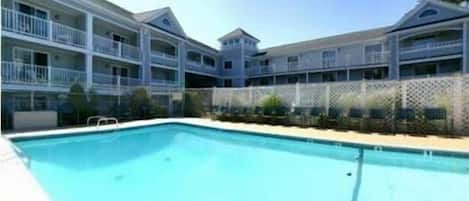 A hotel with a swimming pool, multiple balconies, and a fenced garden area.