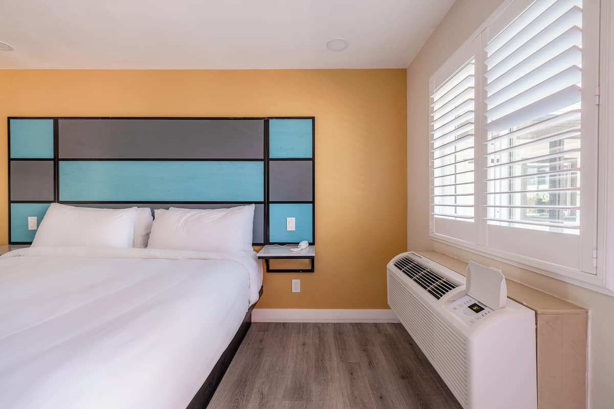 A hotel room with a bed, a nightstand, a heater, and a window with blinds.
