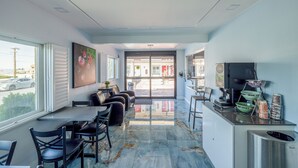 A modern interior with a seating area, a counter with amenities, and a view through a glass door. - Hotel Avenida Victorville I 15 (Victorville)