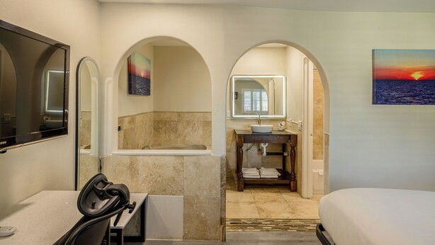 A hotel bathroom with a bathtub, a sink, a mirror, and a painting of a sunset. - Hotel Avenida Victorville I 15 (Victorville)