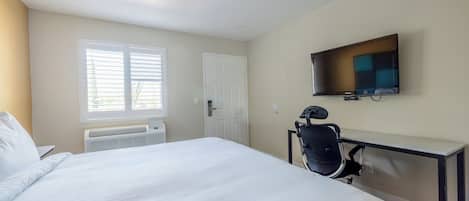 Habitación de hotel con cama, escritorio, silla, televisor y ventana con persianas.