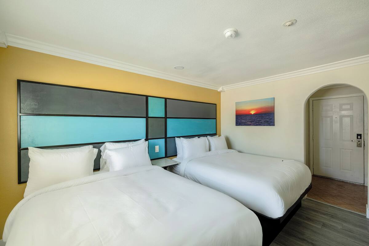 A hotel room with two beds, a large abstract painting on the wall, and a door to the right.