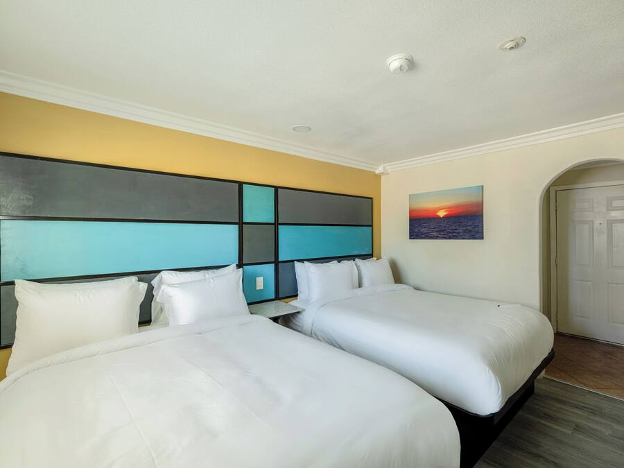 A hotel room with two beds, a large abstract painting on the wall, and a door to the right.