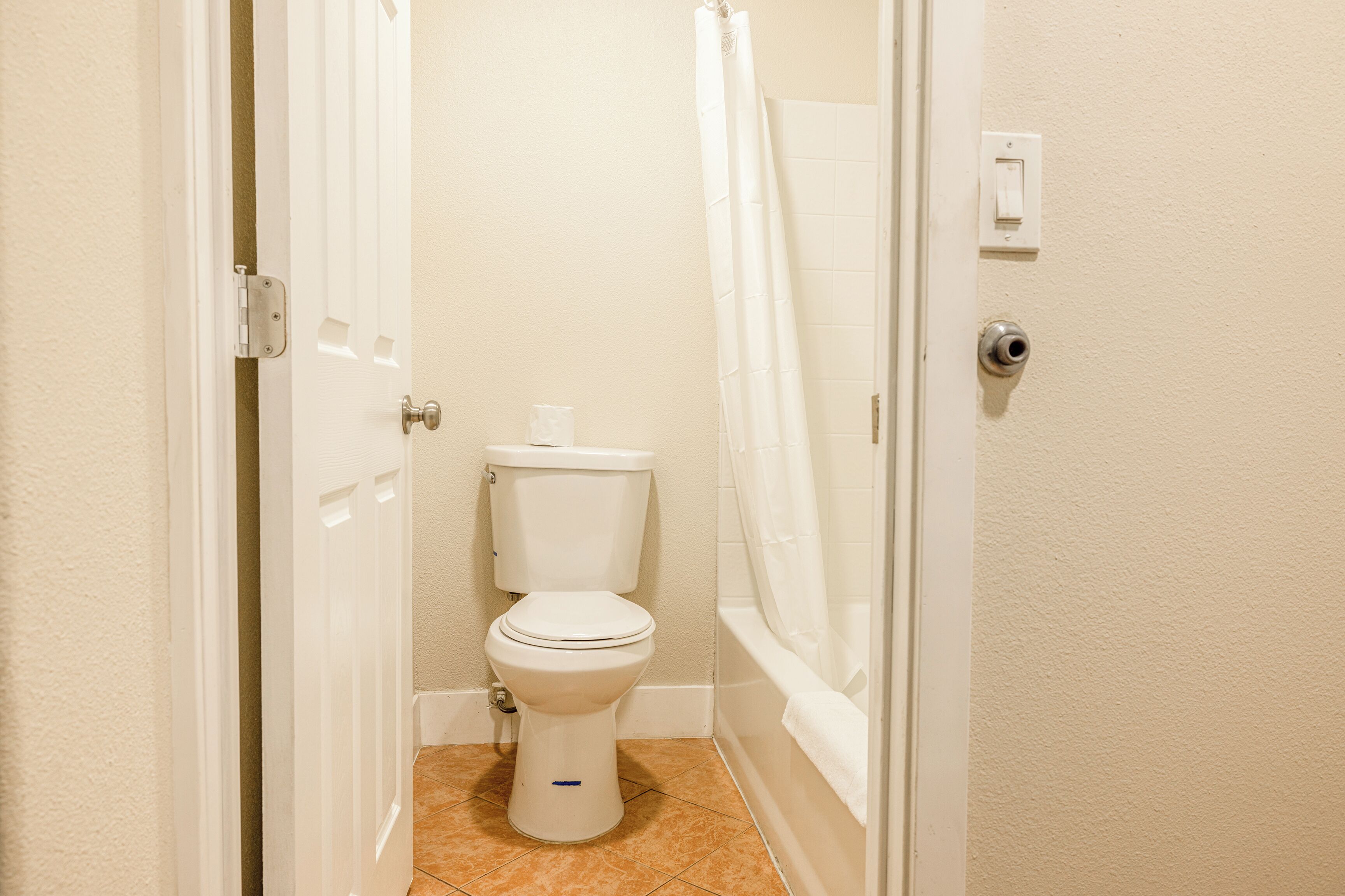 A small, clean bathroom with a toilet, a shower curtain, and a light switch on the wall.