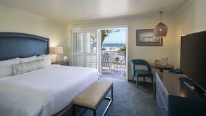 Una habitación de hotel con una cama grande, un banco, un escritorio con una silla, un televisor y vista a la playa.