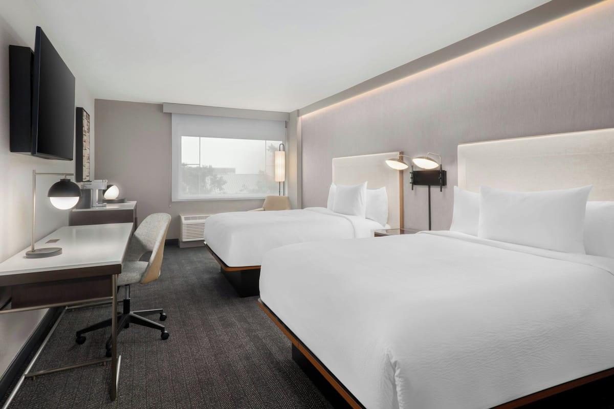 A hotel room with two beds, a desk with a chair, a TV, and a window.