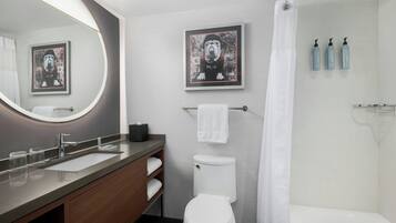 A modern bathroom with a sink, toilet, and shower. There are framed pictures on the wall, a towel rack, and toiletries on the wall.