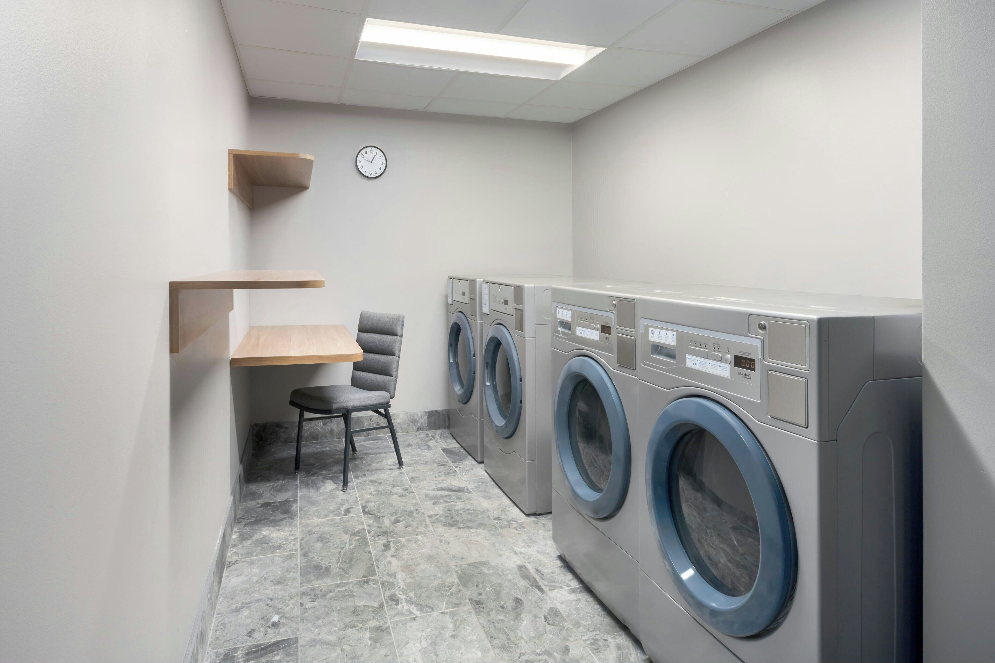 A laundry room with a chair, a small table, and three stacked washing machines.