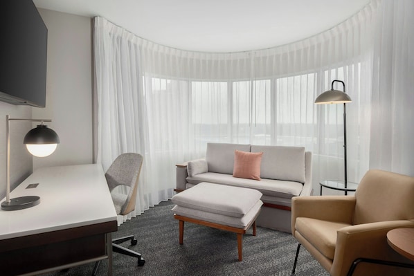 A hotel room with a desk, chair, sofa, ottoman, and a lamp. - Courtyard by Marriott Athens Downtown (Athens)