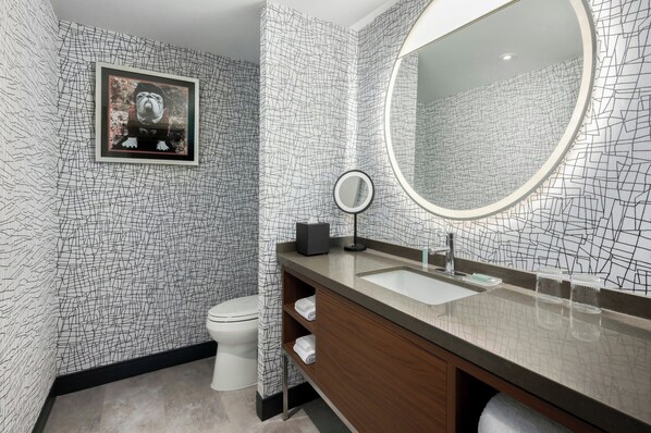 A modern bathroom with a patterned wall, a large mirror, a sink, and a toilet. - Courtyard by Marriott Athens Downtown (Athens)