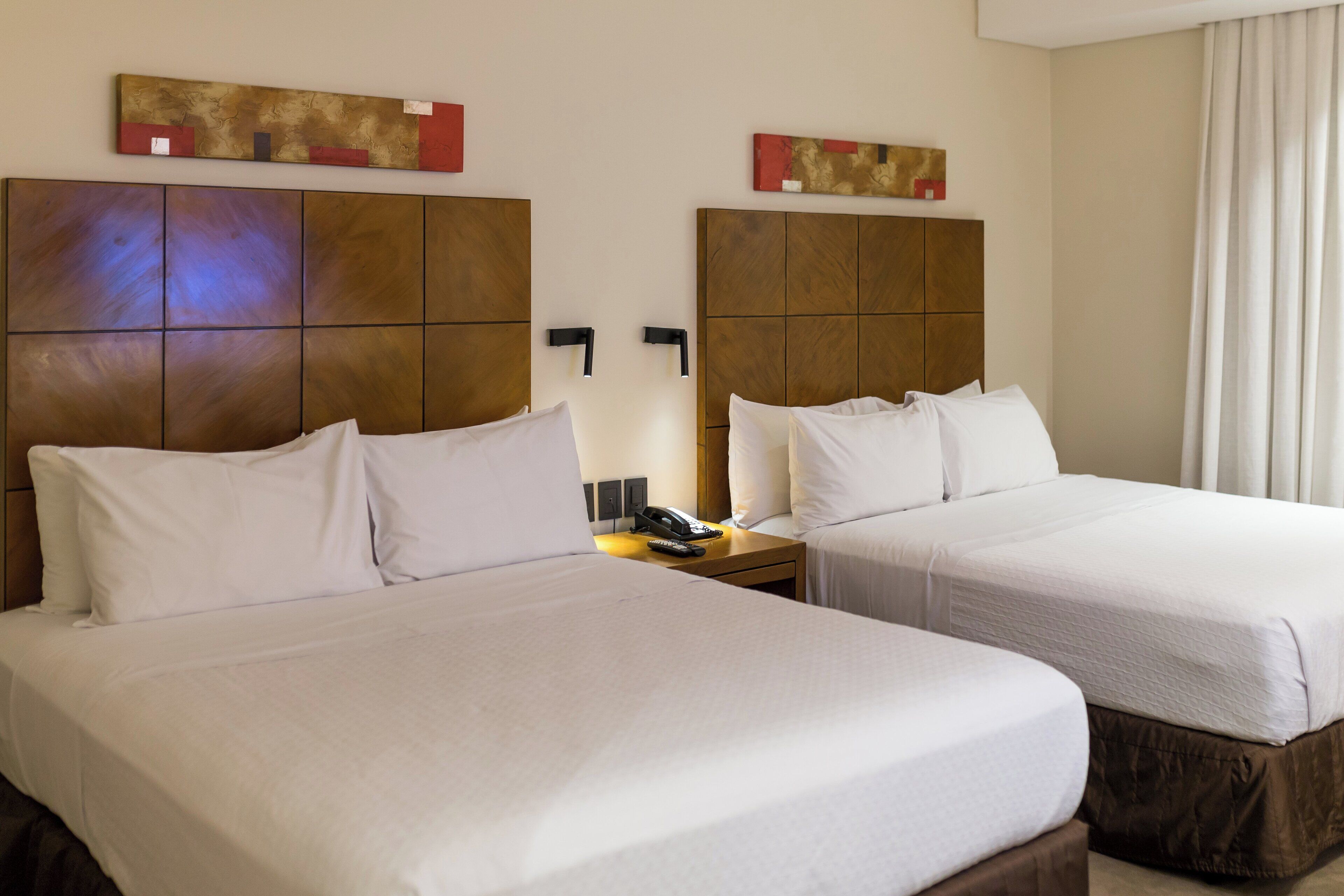 A hotel room with two beds, a nightstand with a phone, and artwork on the walls.