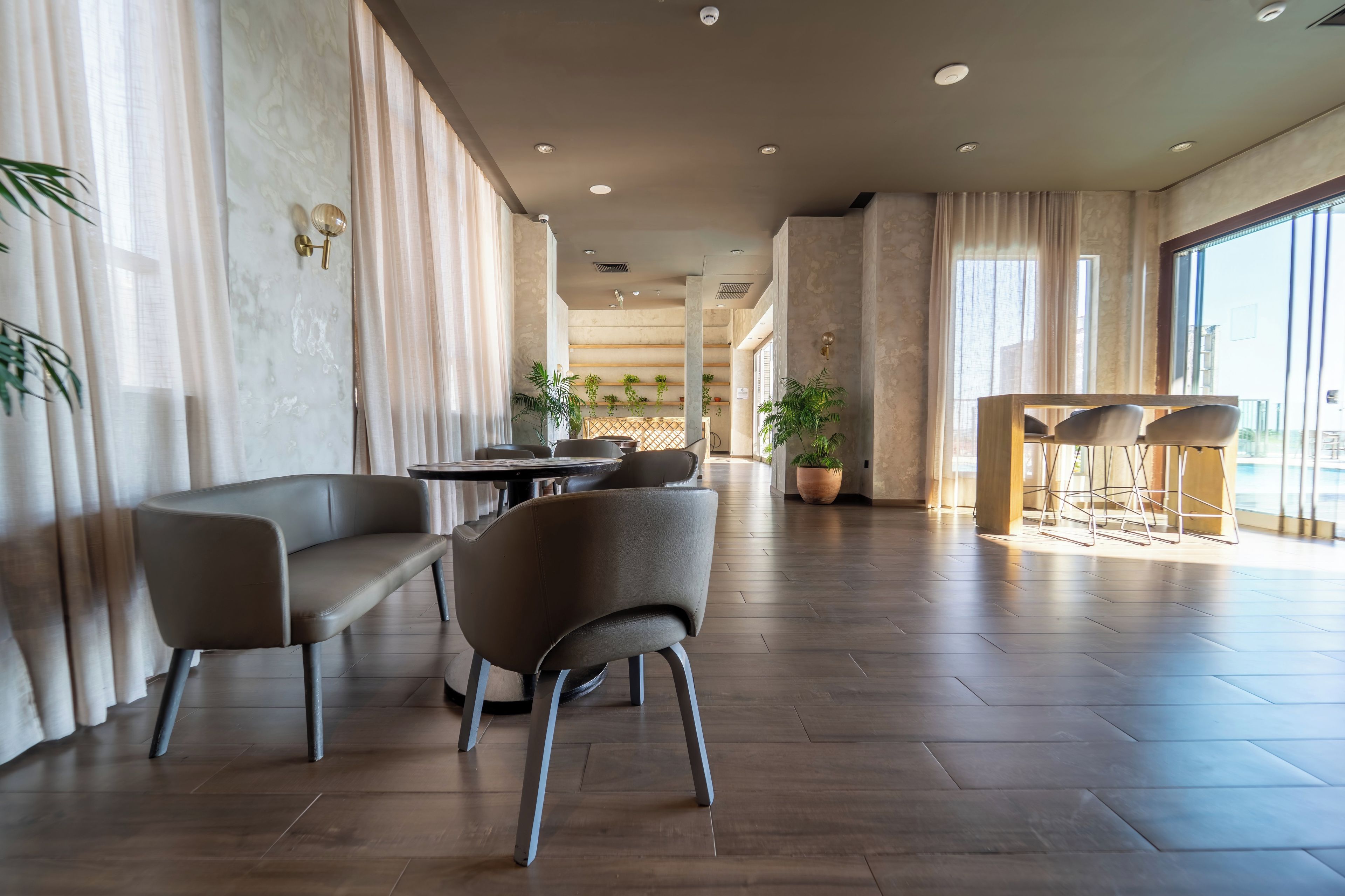 Un amplio vestíbulo de hotel con un diseño moderno, que cuenta con una zona de estar con sofás y sillones, una recepción y grandes ventanales que permiten la entrada de luz natural.