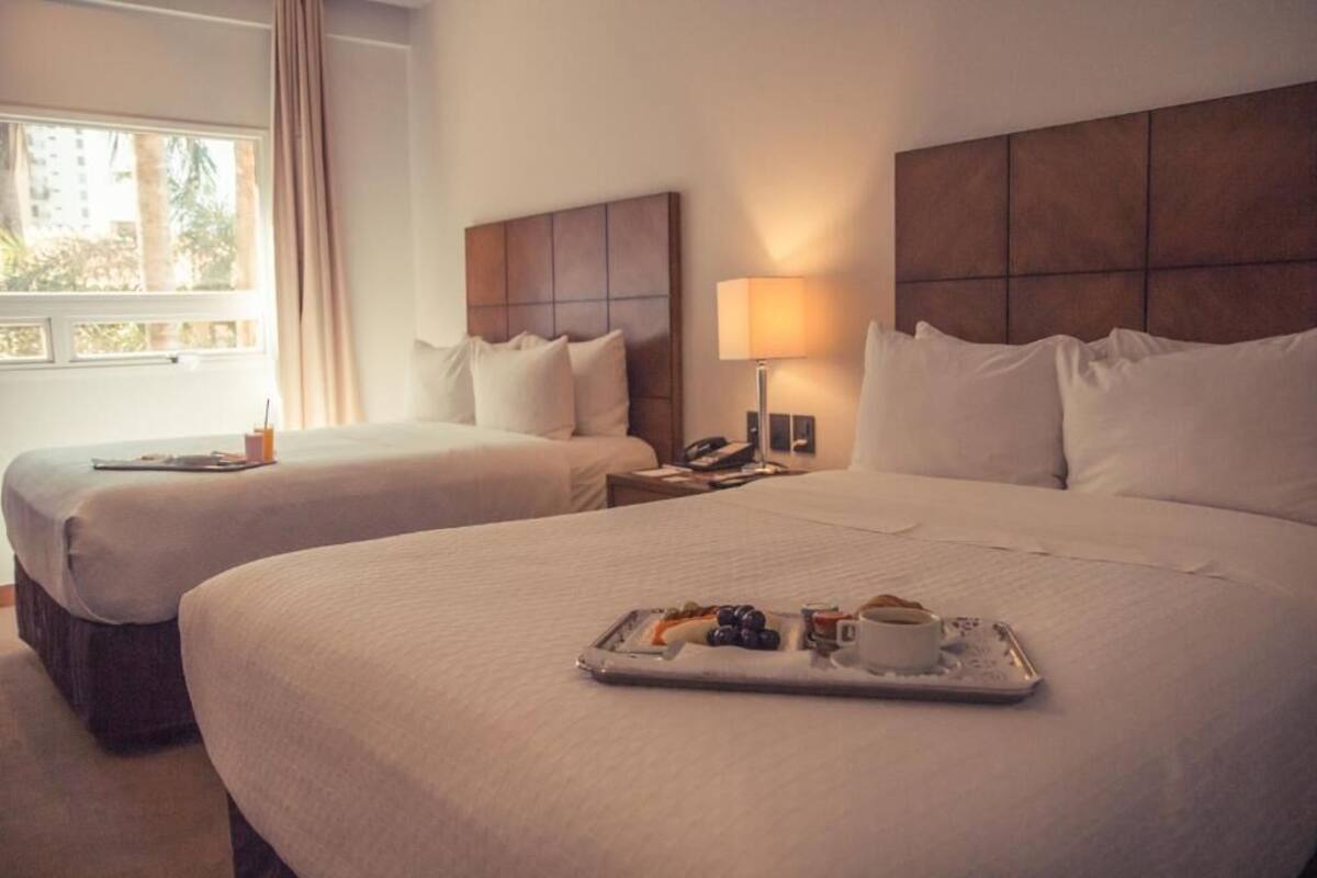 A hotel room with two beds, a bedside table with a lamp, and a tray with breakfast items.