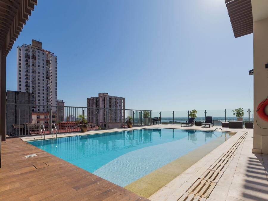 Una piscina sul tetto con acqua cristallina, circondata da un solarium in legno e lettini da relax.