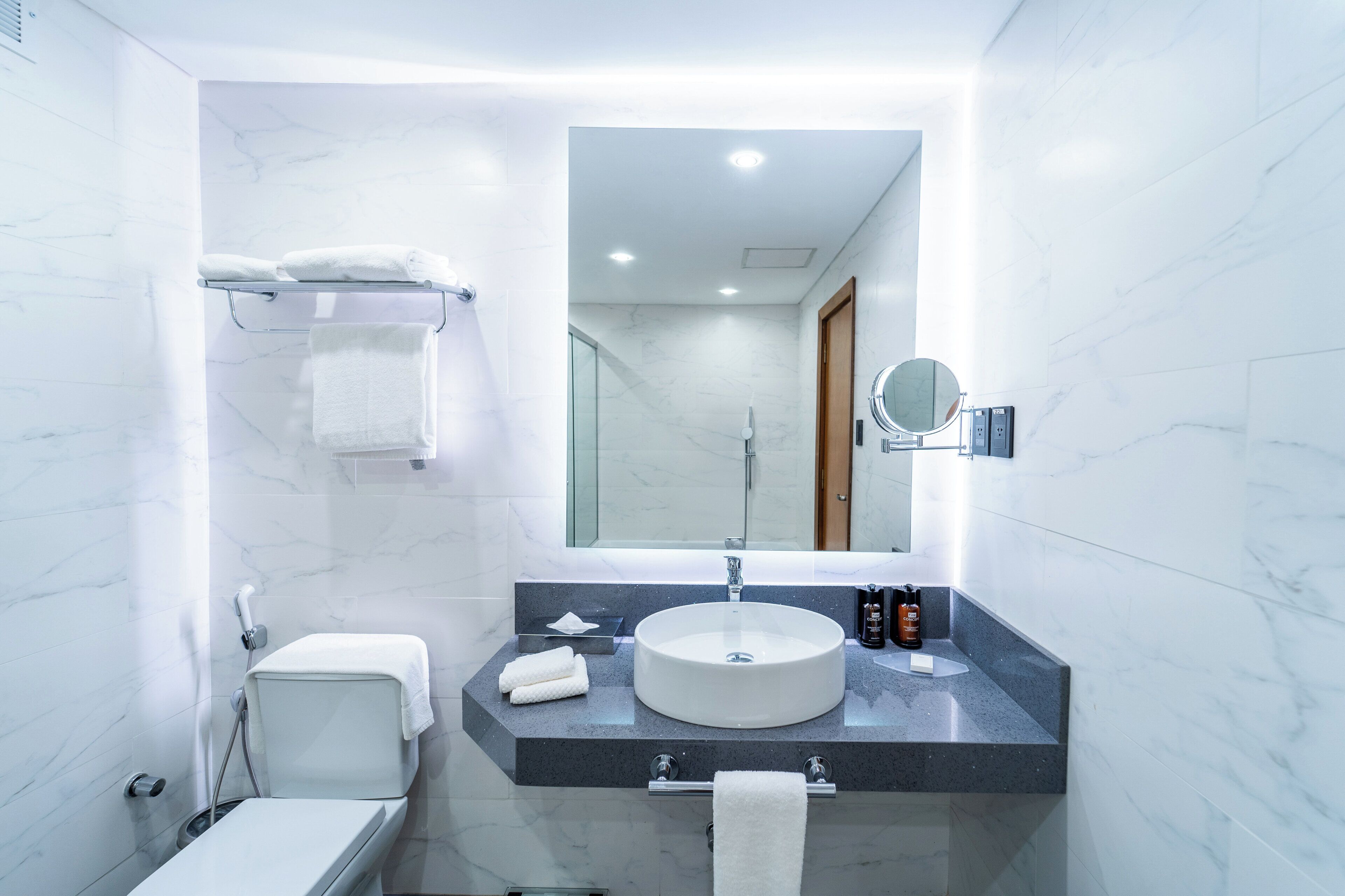 Een moderne badkamer met een marmeren wand, een rond wastafel, toilet en een douchecabine met glazen wanden.