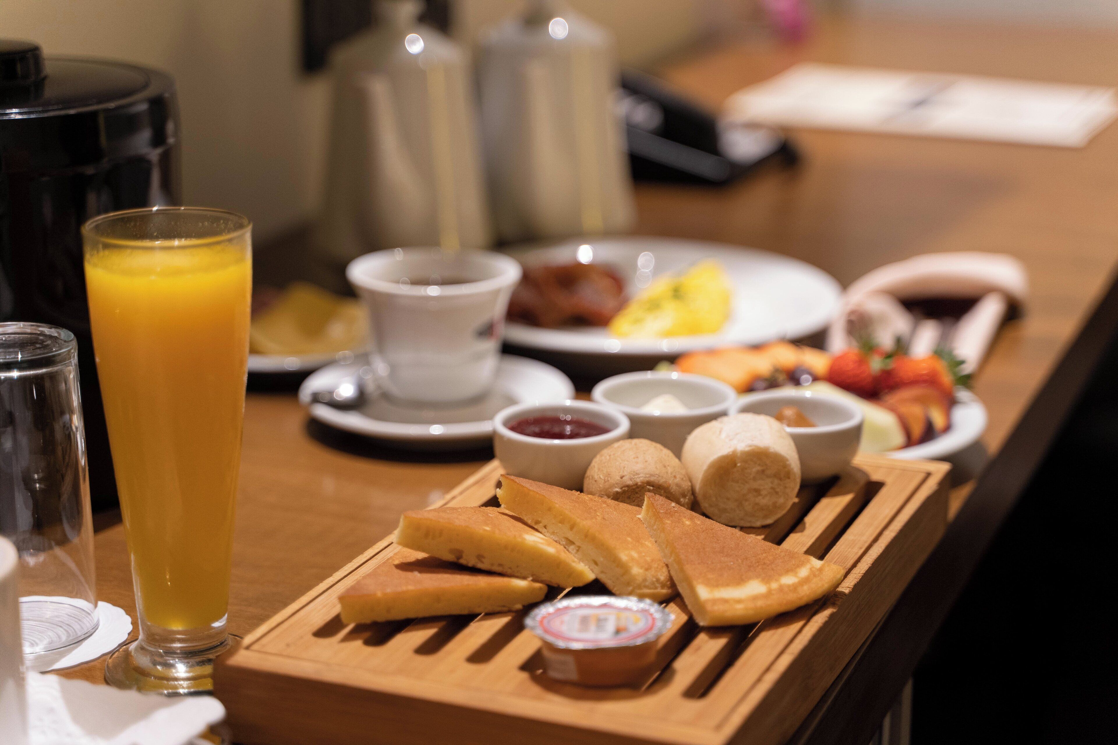 Un plateau de petit-déjeuner avec des toasts, de la confiture et du beurre, le tout disposé sur une planche en bois.