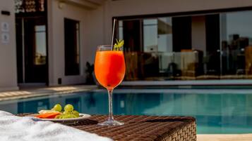 A glass of orange drink with a straw and mint on a wicker table by a pool.