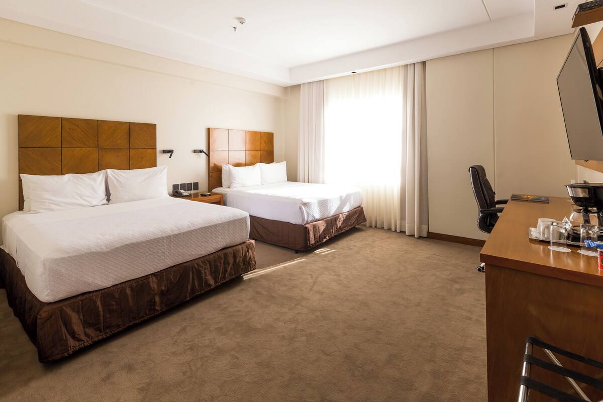 A hotel room with two beds, a desk, and a television.