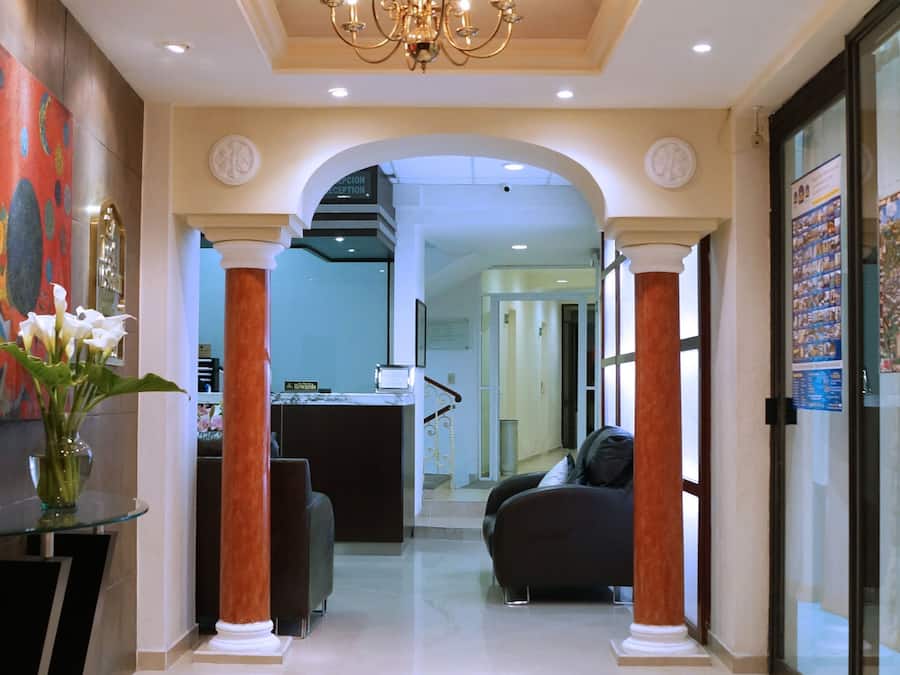 Un hall de hotel con candelabro, columnas, mostrador de recepción y zona de estar.