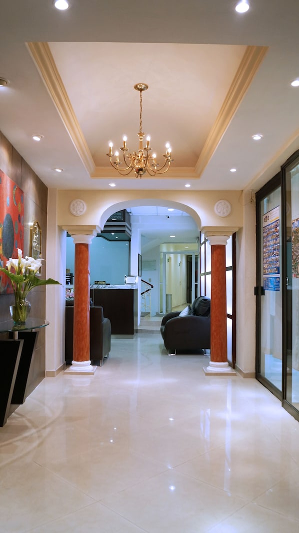 A hotel lobby with a chandelier, columns, a reception desk, and a seating area.