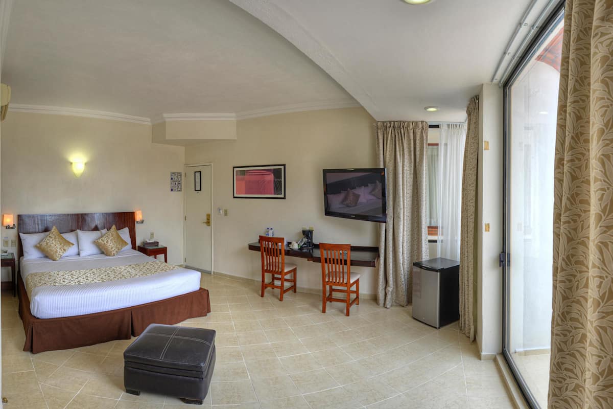 A hotel room with a large bed, a desk with a chair, a television, and a minibar.