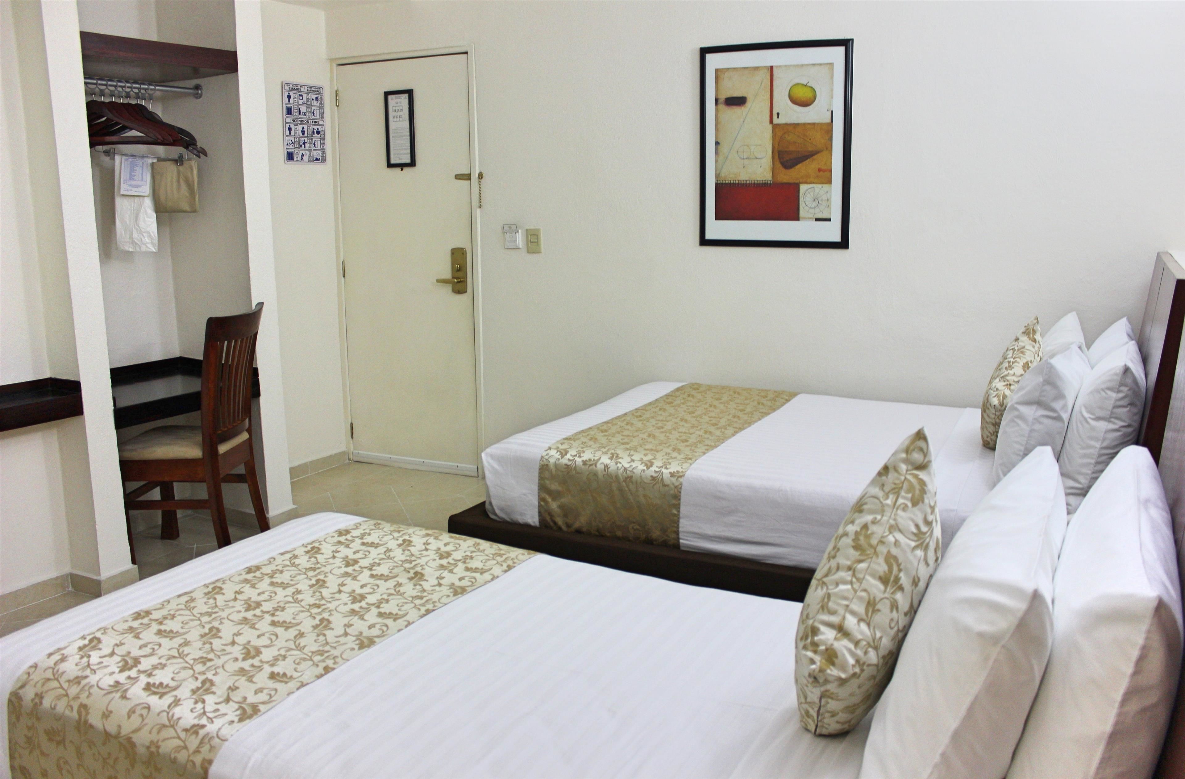 A hotel room with two beds, a chair, a coat rack, and a door.