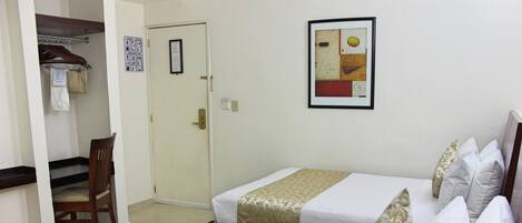 A hotel room with two beds, a chair, a coat rack, and a door.