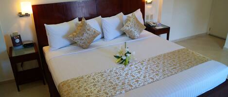 A neatly made bed with a floral bedspread, a bouquet of white flowers, and a wooden headboard.