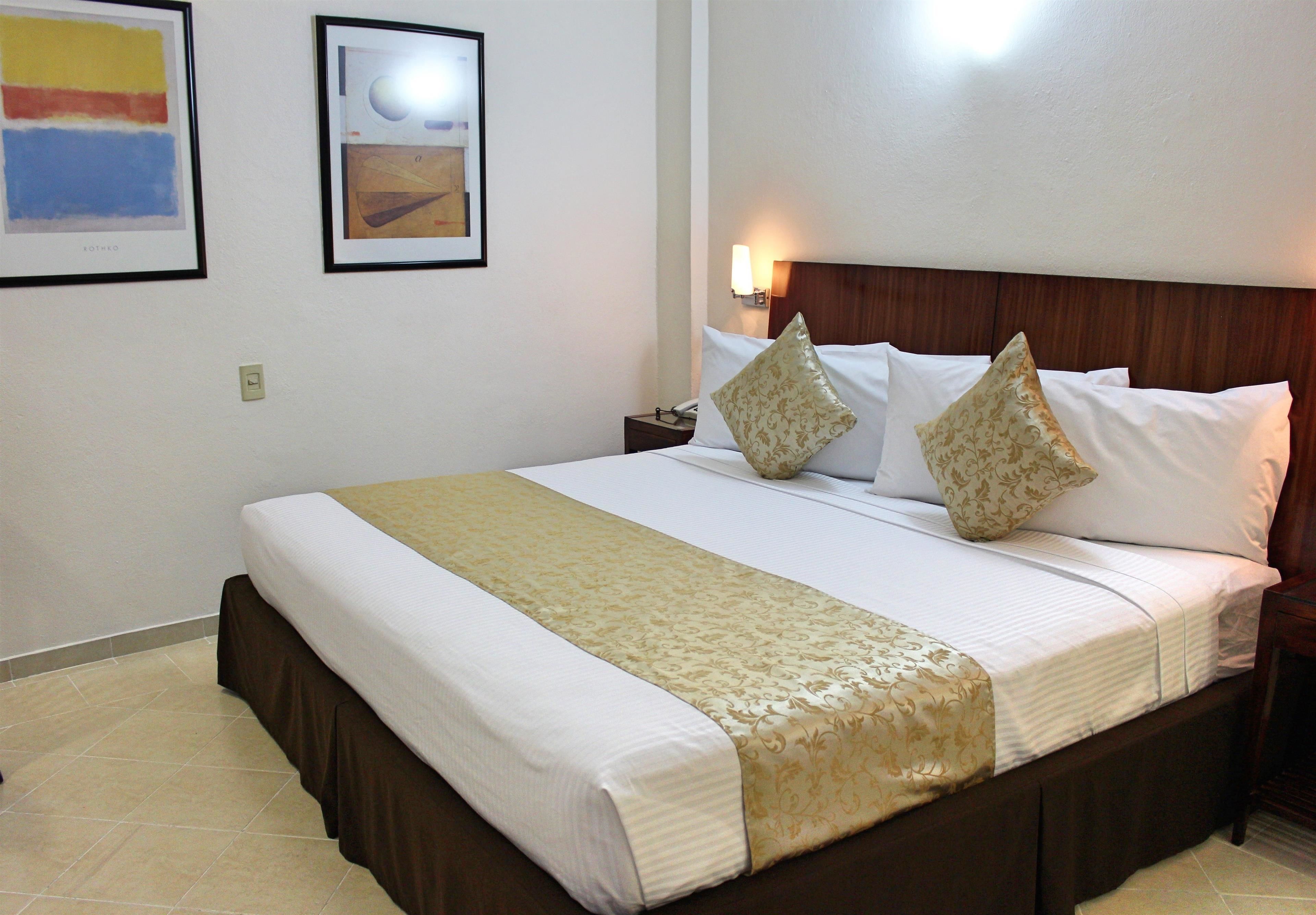 A neatly made bed with a brown skirt, white linens, and two decorative pillows.