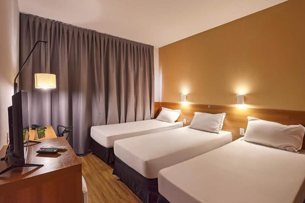 A hotel room with three beds, a desk with a computer, and a lamp.