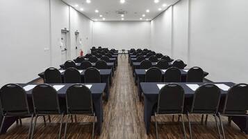 A conference room with rows of black chairs and tables, white walls, and a wooden floor.