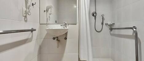 Un baño con lavamanos, secamanos, ducha con barra de apoyo y suelo de madera.