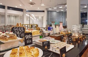Un bufé con diversos alimentos y etiquetas, incluyendo 'Gula Doa' y 'Geleia'.