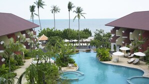 A resort pool area with a view of the sea, surrounded by palm trees and lounge chairs. - Bella Villa Cabana (Pattaya)