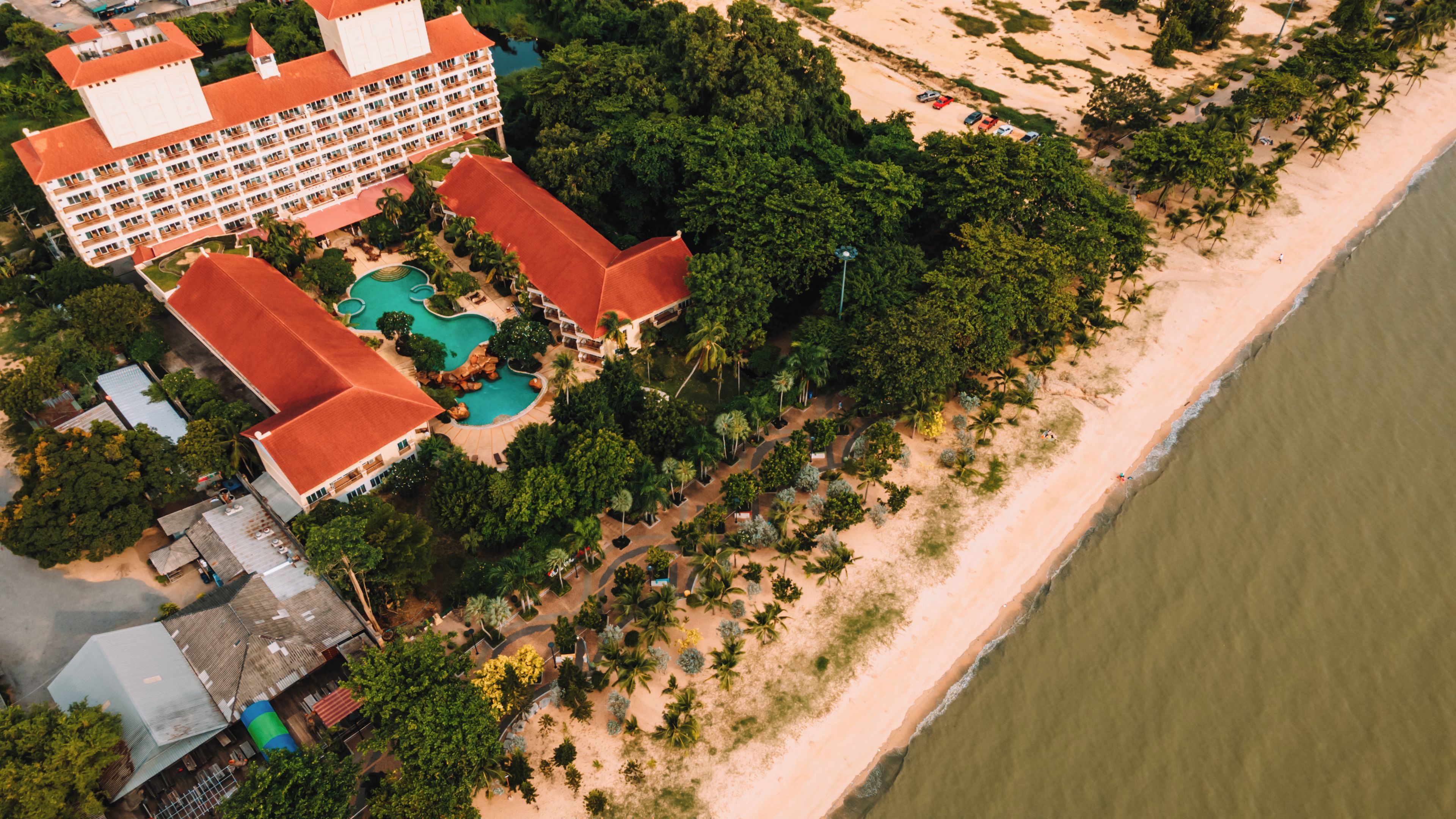 An aerial view of a resort with a large building, multiple pools, and a beachfront.