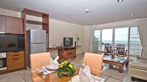 A modern hotel room with a dining area, a kitchen, and a balcony with a view of the ocean. - Bella Villa Cabana (Pattaya)