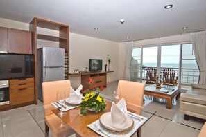 A modern hotel room with a dining area, a kitchen, and a balcony with a view of the ocean. - Bella Villa Cabana (Pattaya)