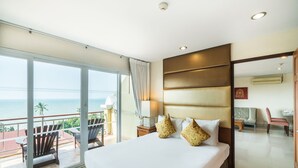 Habitació d'hotel amb un llit gran, un balcó amb vista al mar i una zona de seients separada amb una cadira i una taula.