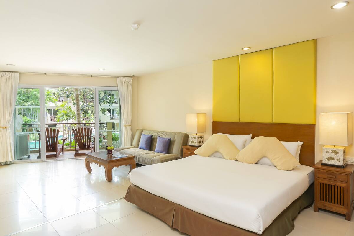 A hotel room with a large bed, a sofa, a small table, and a nightstand with lamps.