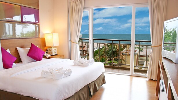 A hotel room with a large bed, a nightstand with a lamp, a TV, and a balcony with a view of the ocean. - Bella Villa Cabana (Pattaya)