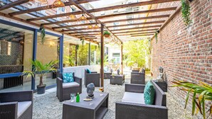An outdoor patio area with wicker furniture, a stone statue, and hanging plants. - Best Western Hotel Saint Claude (Peronne)