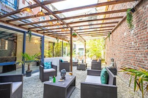 Un patio al aire libre con mobiliario de mimbre, una estatua de piedra y plantas colgantes.