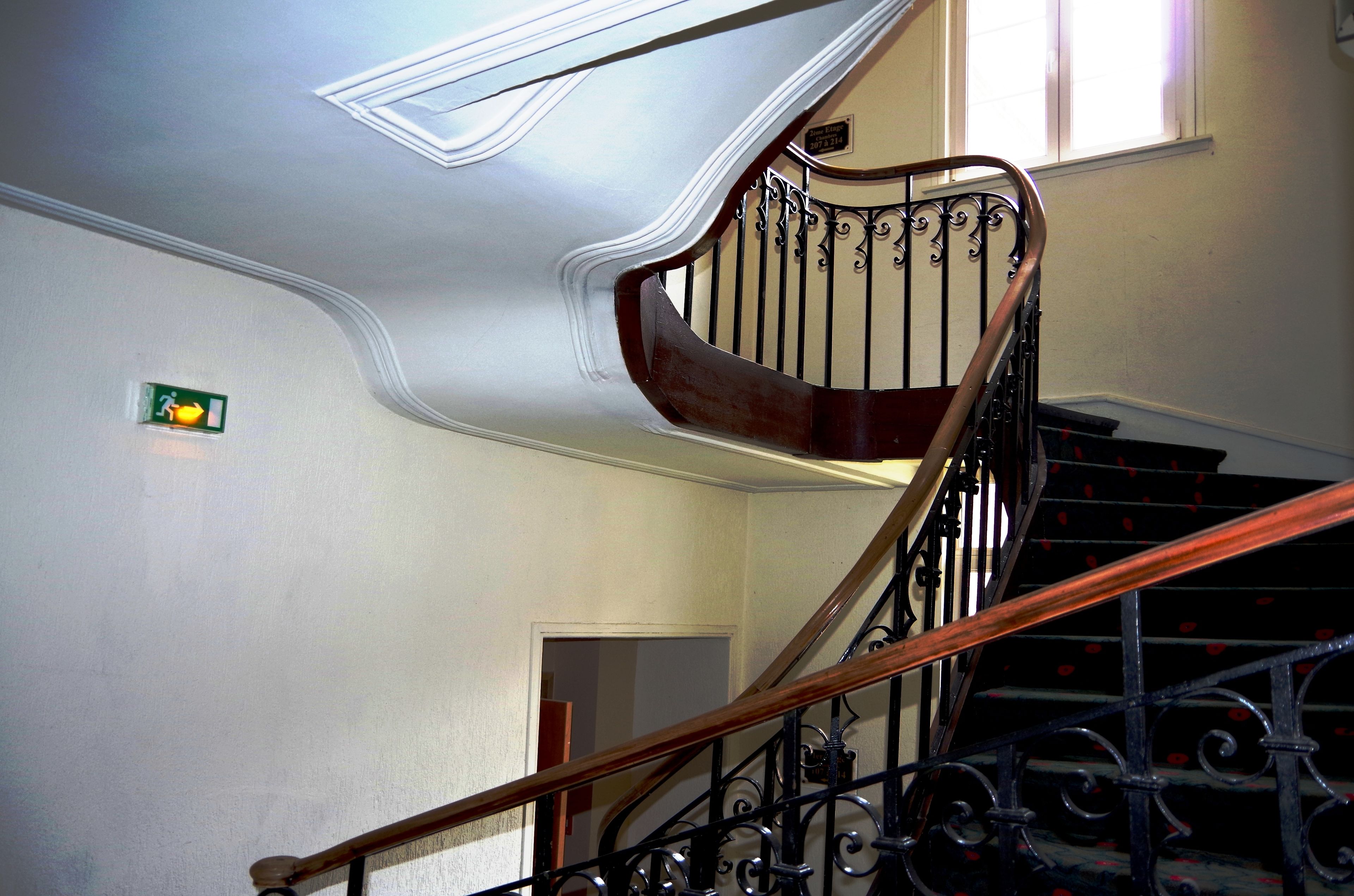 Una escalera con barandillas metálicas ornamentadas y un pasamanos de madera, que conduce a un piso superior.