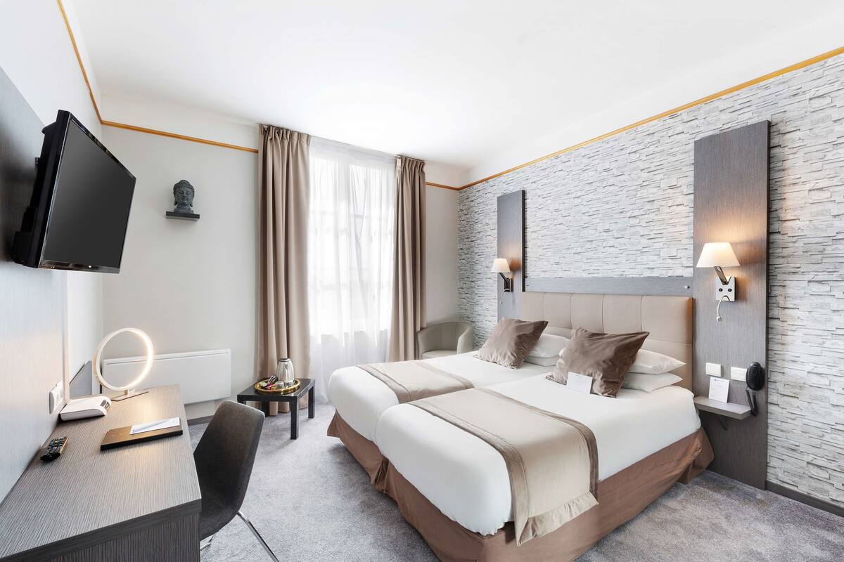 Ein modernes Hotelzimmer mit einem großen Bett, einem Schreibtisch mit Spiegel, einem Flachbildfernseher und einer Wand mit Steinoptik.