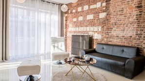 A modern living room with a brick wall, a black leather sofa, a white armchair, a glass coffee table, and pendant lights. - Best Western Hotel Saint Claude (Peronne)