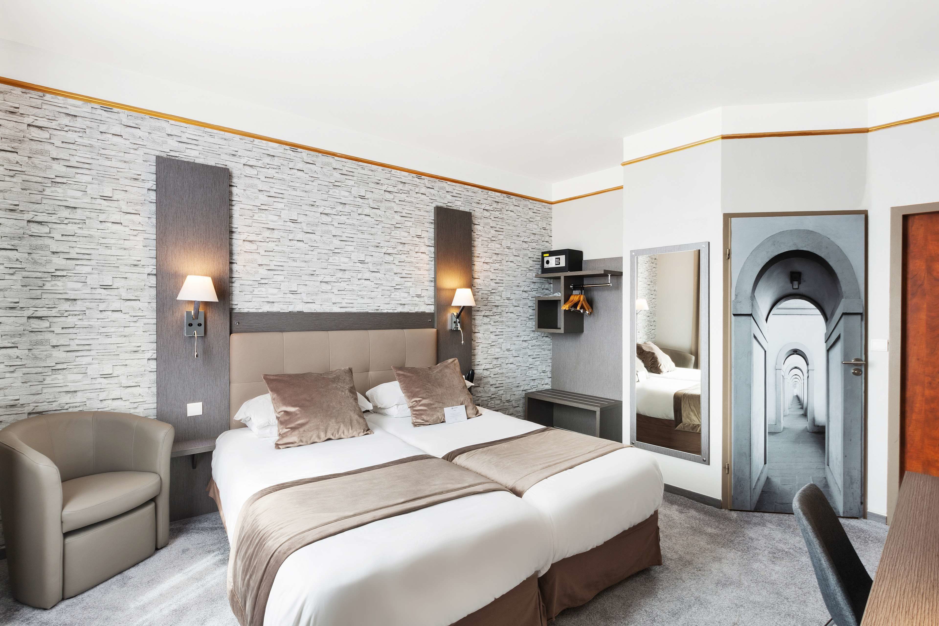 Una camera d'albergo moderna con un letto grande, due lampade ai comodini, una TV integrata e uno specchio che riflette un corridoio.