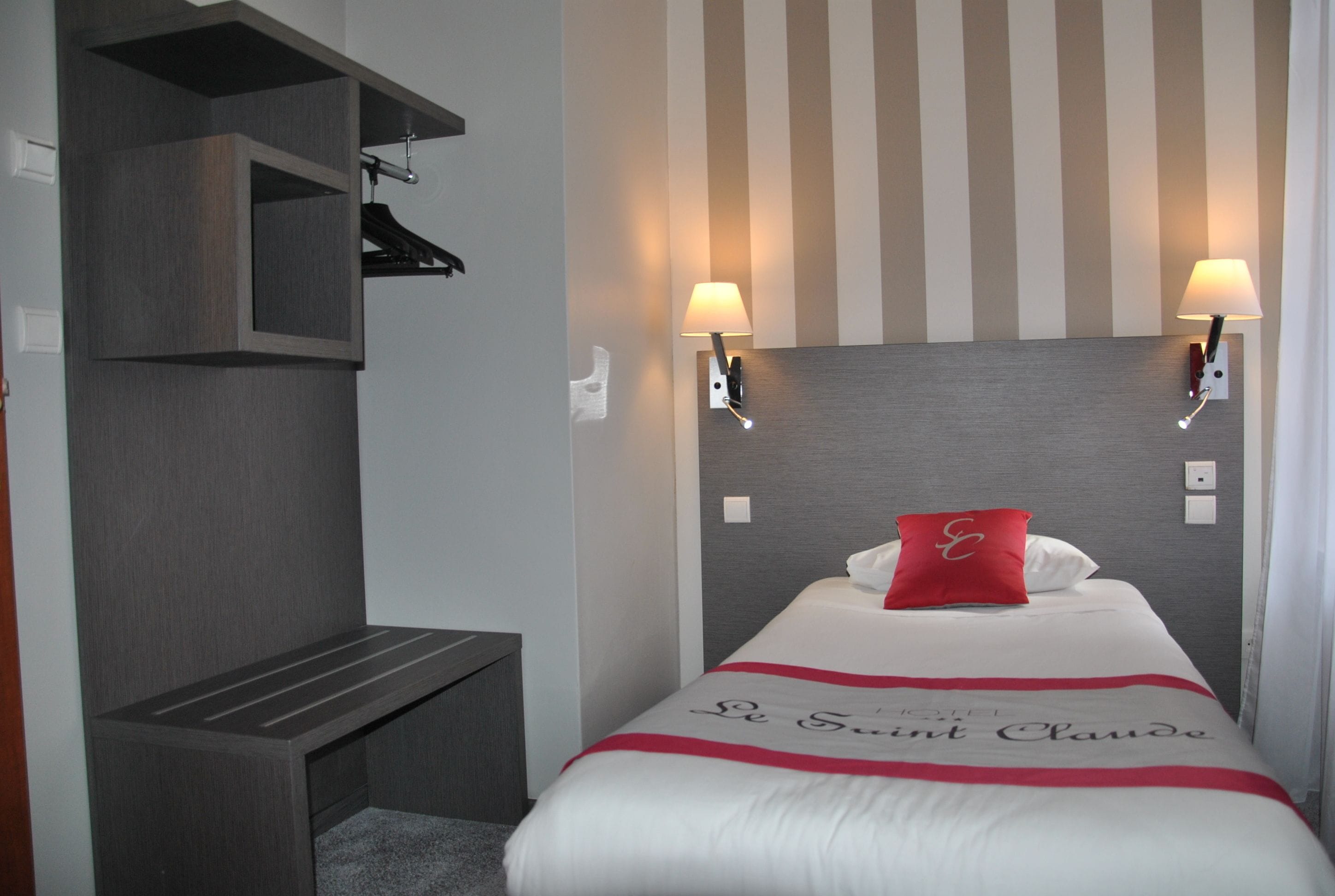 A hotel room with a bed, two wall-mounted lamps, a small bench, and a wardrobe.